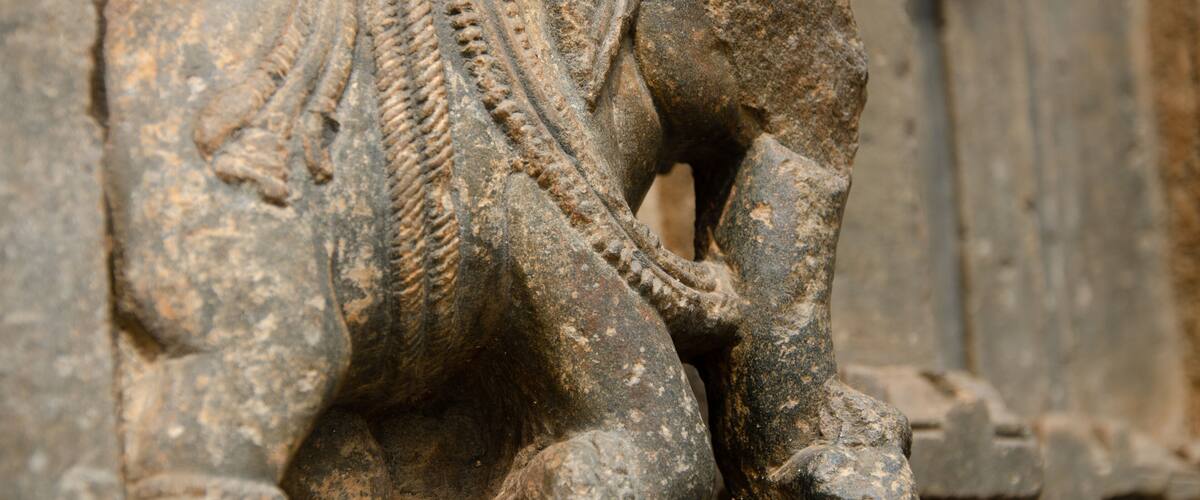 A weathered stone elephant sculpture with intricate carvings and a rope around its neck.