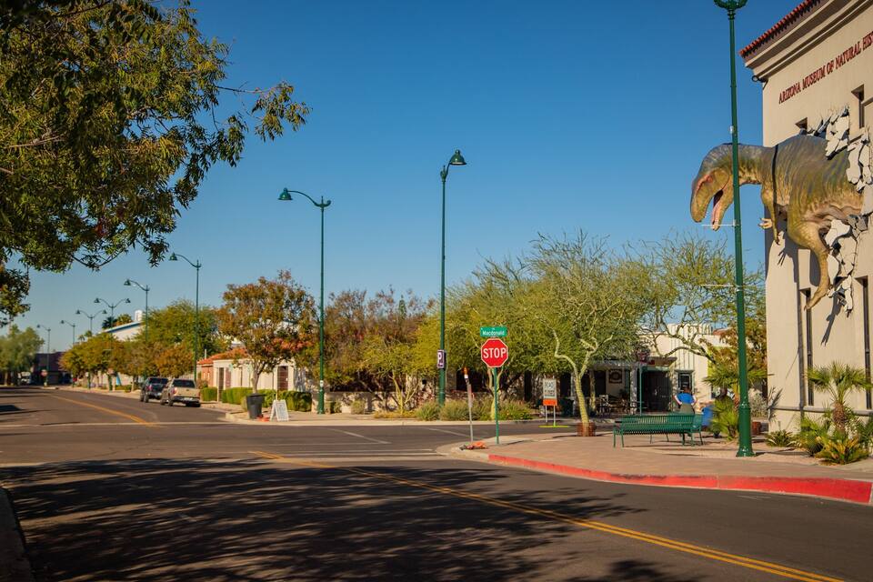 A street with a stop sign, a large dinosaur sculpture, and a building labeled "Arizona Museum of Natural History."