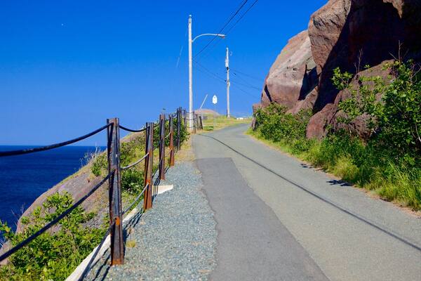 A coastal road with a guardrail, power lines, and a rocky cliff.