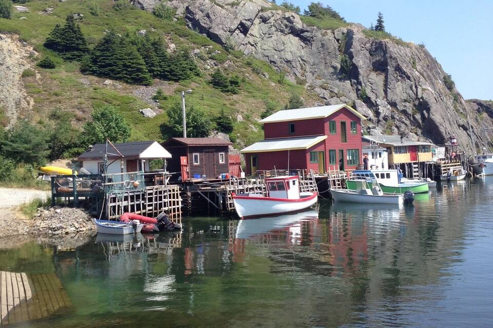 A harbor with boats, a red building, and a rocky hillside.