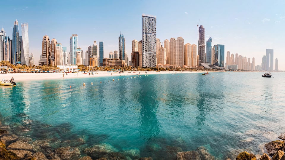 Wide panorama of the Persian Gulf with sandy beach and Bluewaters Island with the worlds famous largest Ferris wheel Dubai Eye and numerous skyscrapers with hotels and residences