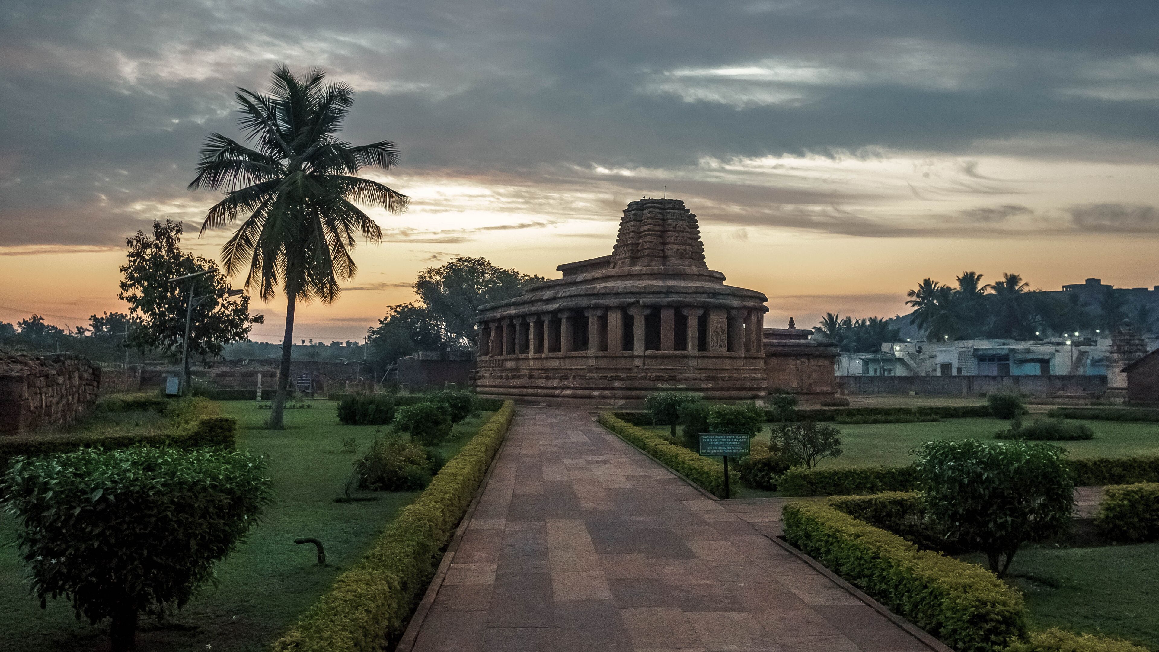A temple with a central tower, surrounded by a well-maintained garden with a pathway leading to it.