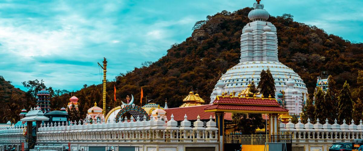 A white temple with a red roof, surrounded by a white fence, and a mountain in the background.