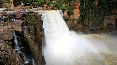 Uma grande cachoeira com um arco-íris, cercada por penhascos rochosos e vegetação.