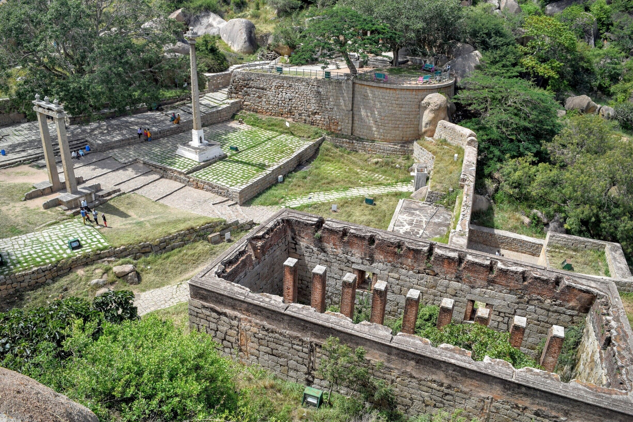 An ancient archaeological site with stone structures, a large stone lion, and a paved area with visitors.