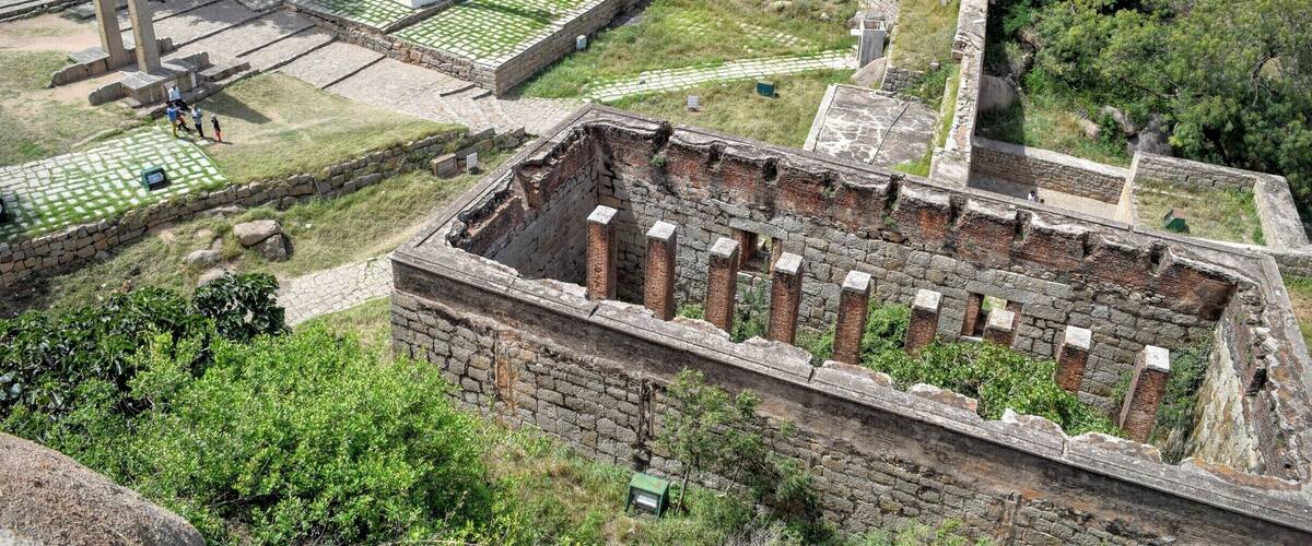 An ancient archaeological site with stone structures, a large stone lion, and a paved area with visitors.