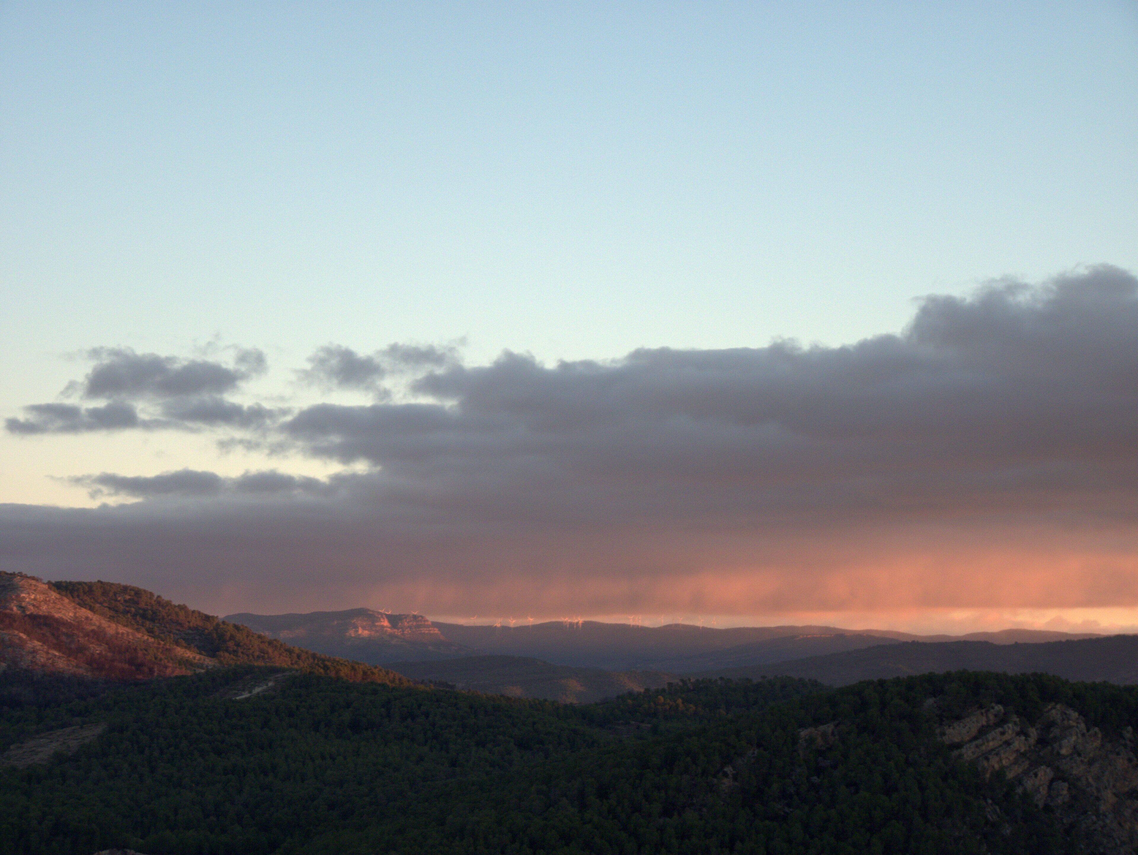 A mountainous landscape with dense forests and a cloudy sky.
