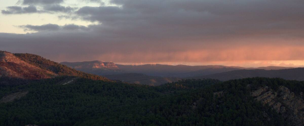A mountainous landscape with dense forests and a cloudy sky.