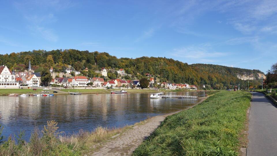 A riverside town with historic buildings, boats, and a pathway along the water.