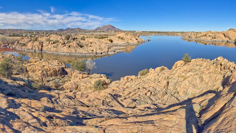 A rocky landscape with a calm lake, mountains in the background, and sparse vegetation.