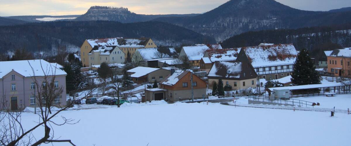 A snow-covered village with houses and a prominent mountain in the background.