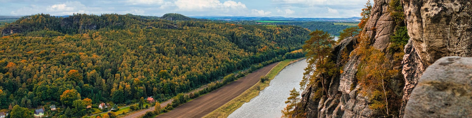 A river flowing through a valley with a rocky cliff on the right and a forested hill on the left.