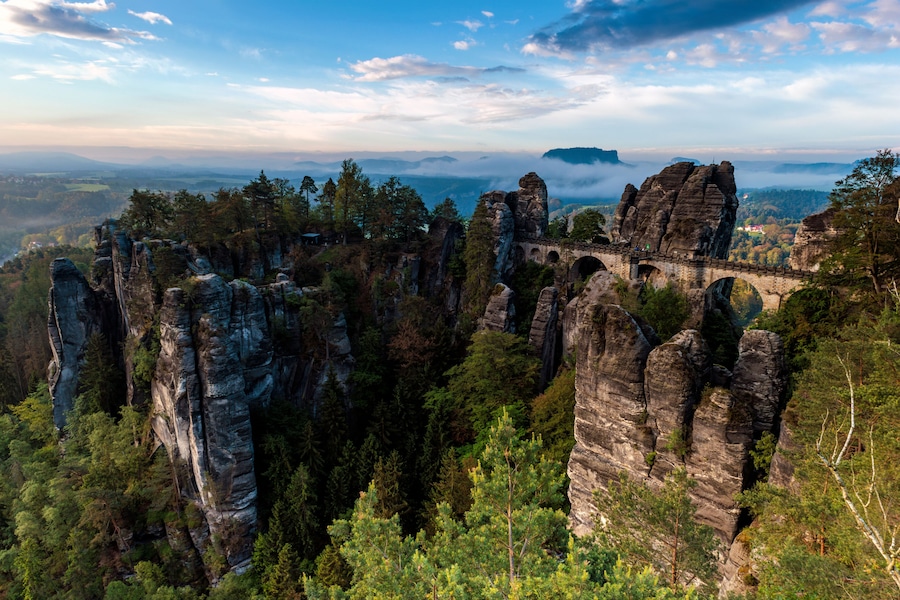 A landscape with rock formations, a bridge, and a forested valley.