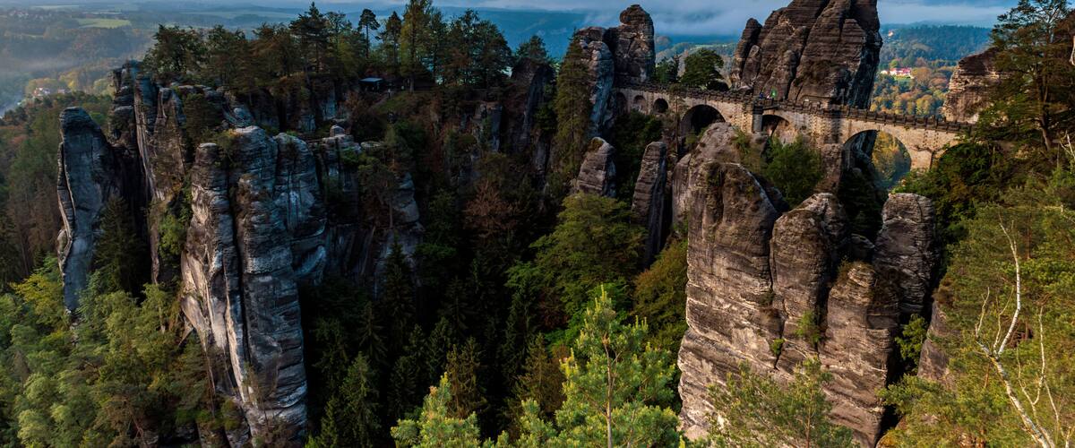 A landscape with rock formations, a bridge, and a forested valley.