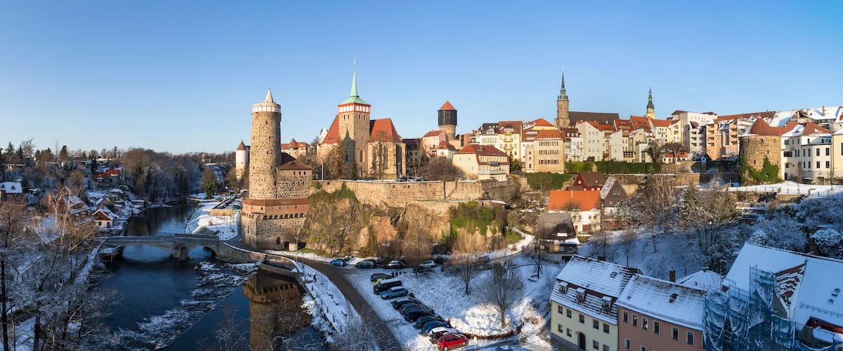 Eine historische Stadt mit Burg, Fluss und schneebedeckten Häusern.