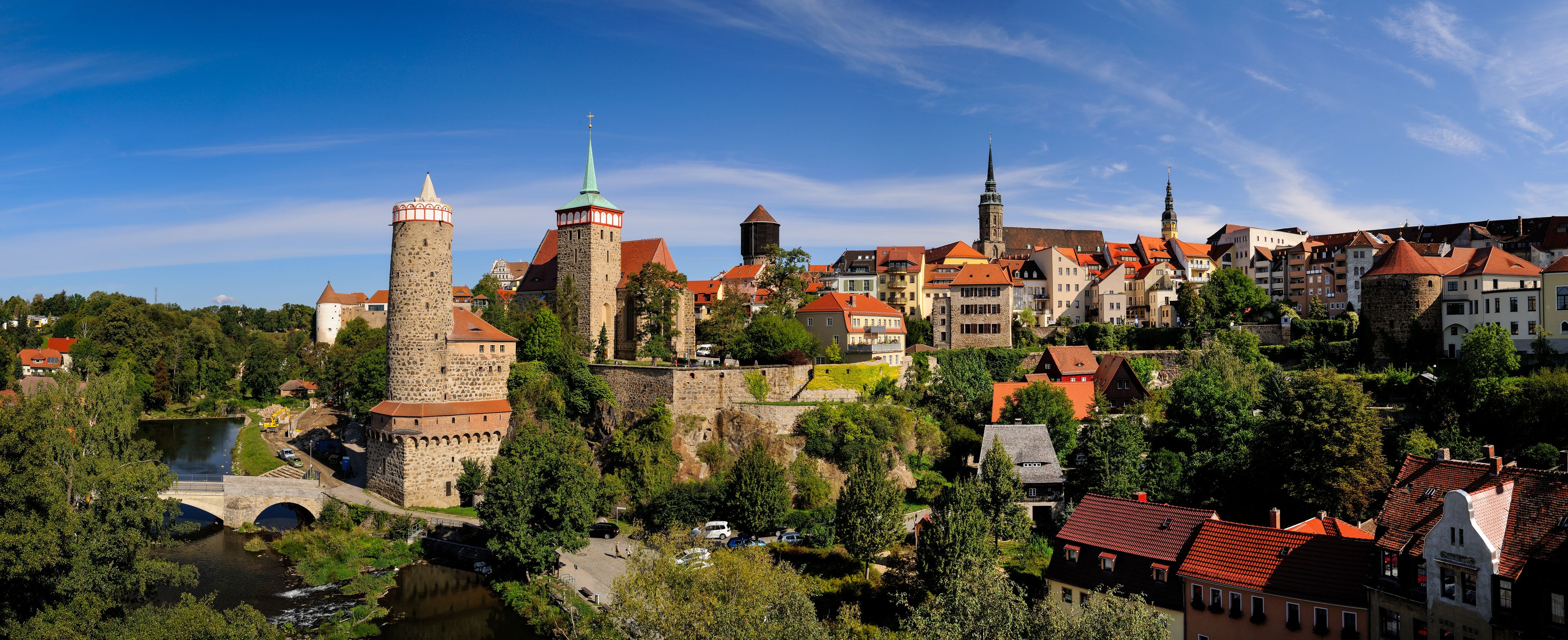 A historic town with a prominent castle, a church with a tall spire, and a river flowing through the center.