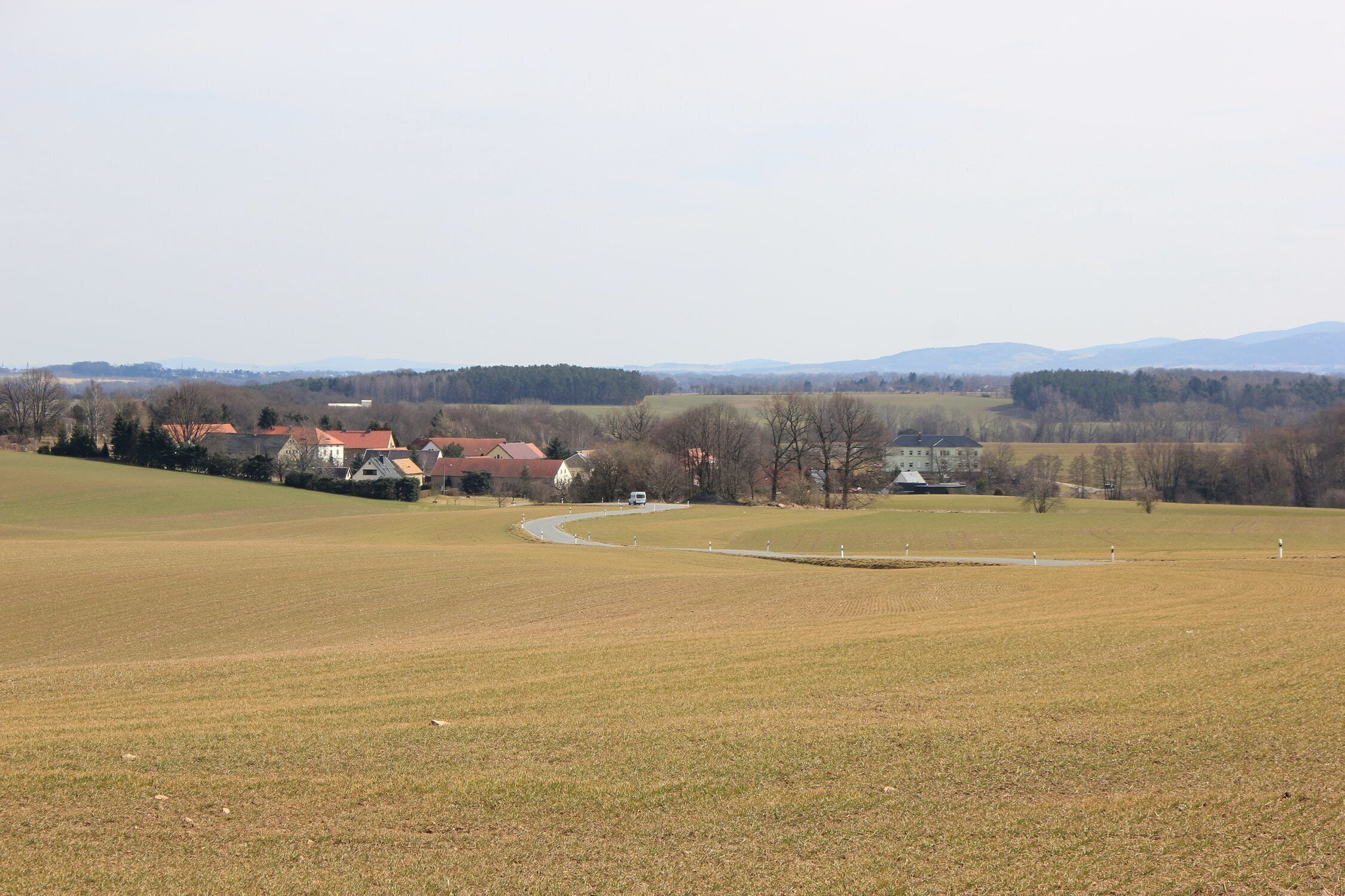 A rural landscape with rolling hills, a winding road, and scattered houses with red roofs.
