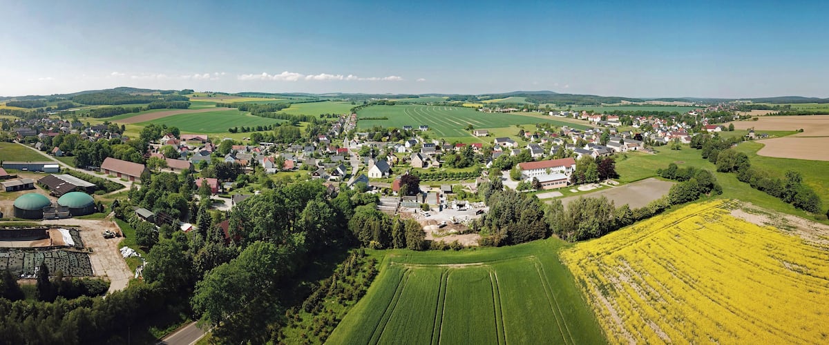 An aerial view of a rural village with green fields, a central cluster of houses, and a large green dome structure.