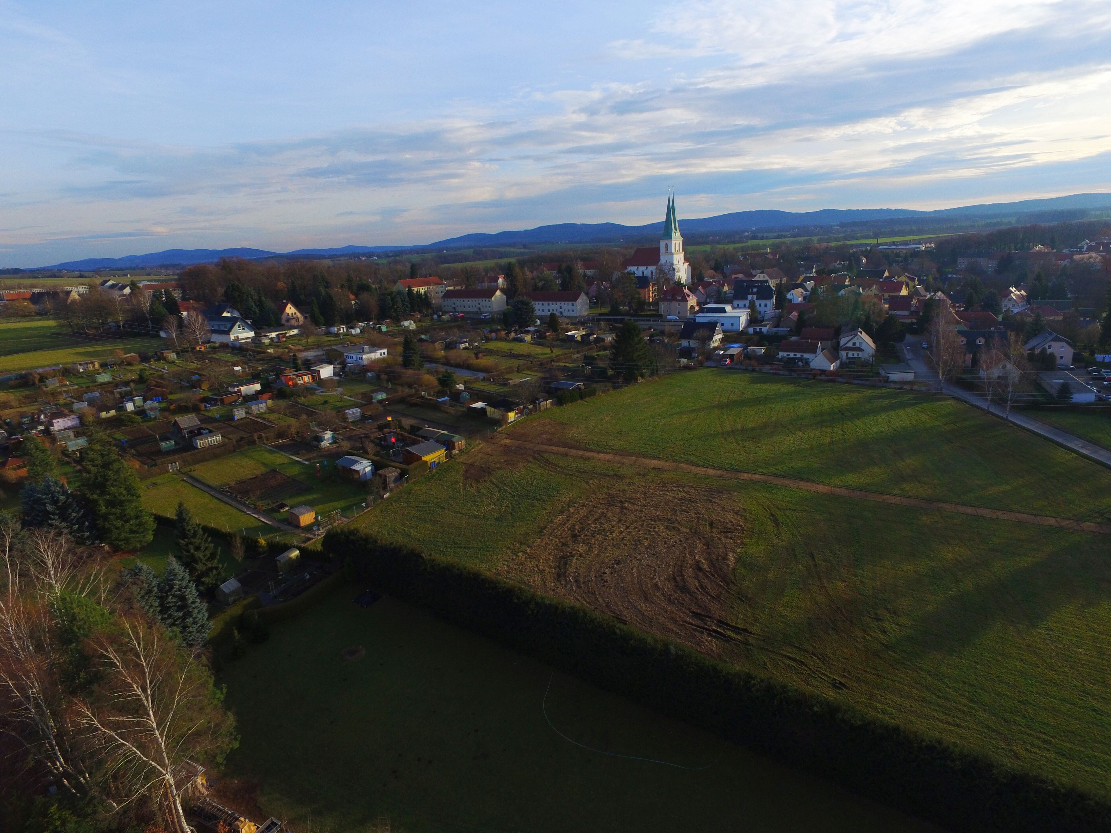 Vista aérea de un pueblo con una iglesia destacada, campos verdes y casas dispersas.