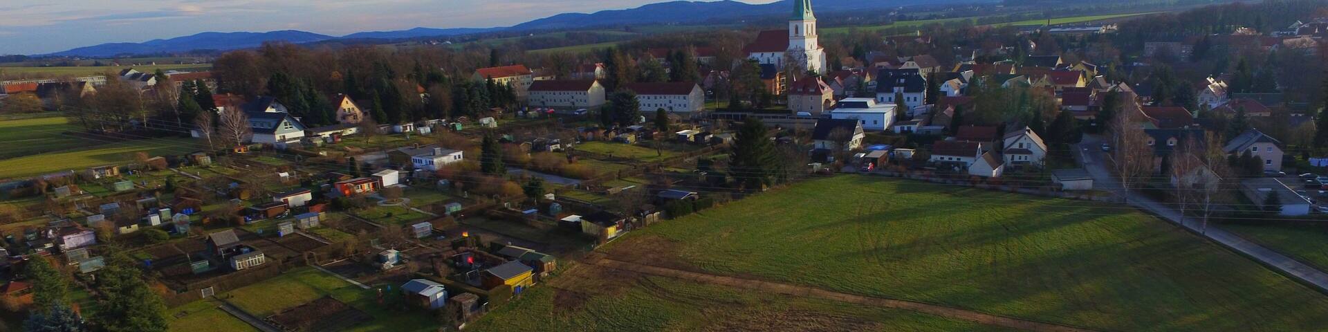 An aerial view of a town with a prominent church, green fields, and scattered houses.