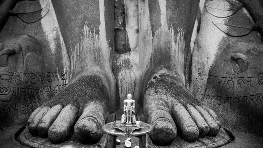 A statue of a deity with inscriptions on the hands and feet, surrounded by a circular base.