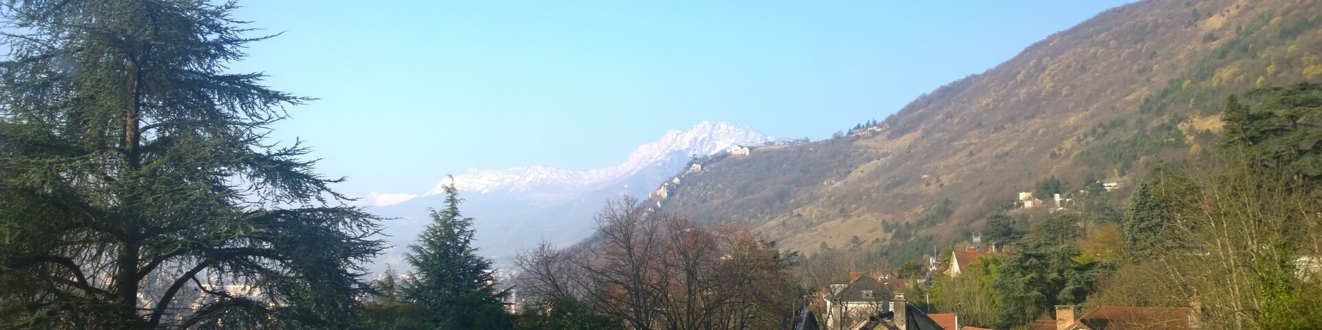 A mountainous landscape with a snow-capped peak, dense forest, and a historic building with a red roof.