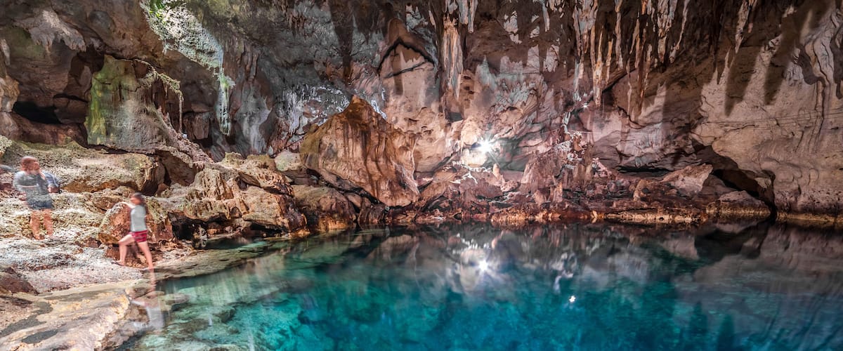 Una cueva con agua cristalina, formaciones rocosas y gente explorando.