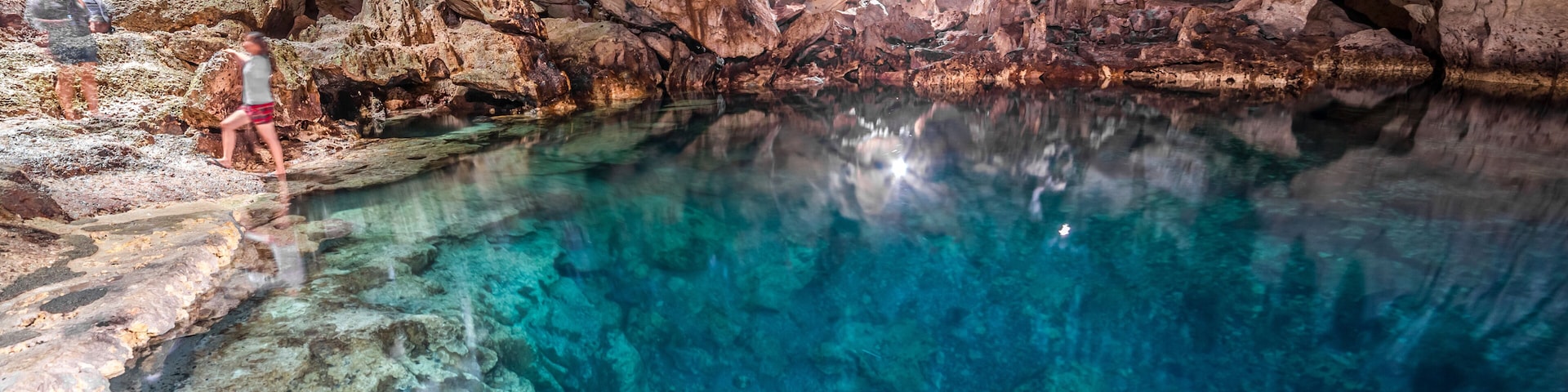 Una cueva con agua cristalina, formaciones rocosas y gente explorando.