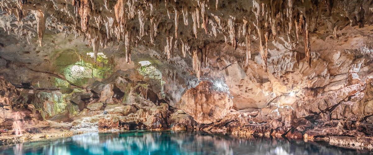 A cave with stalactites, clear water, and a rocky bottom.