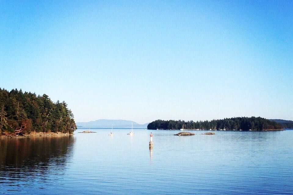A calm lake with a forested island and a lighthouse in the distance.
