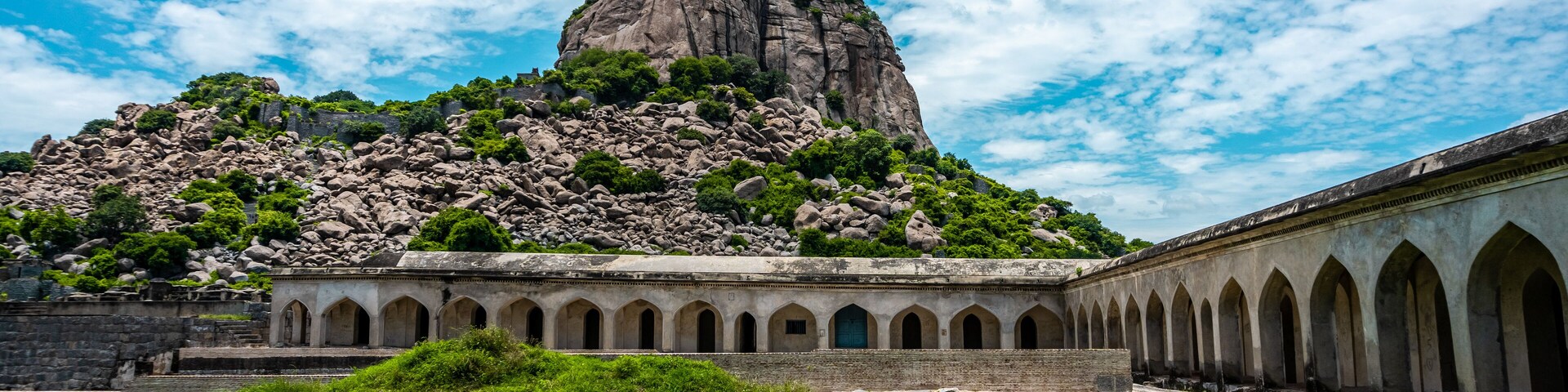 Um edifício histórico com um pátio e uma grande formação rochosa ao fundo.