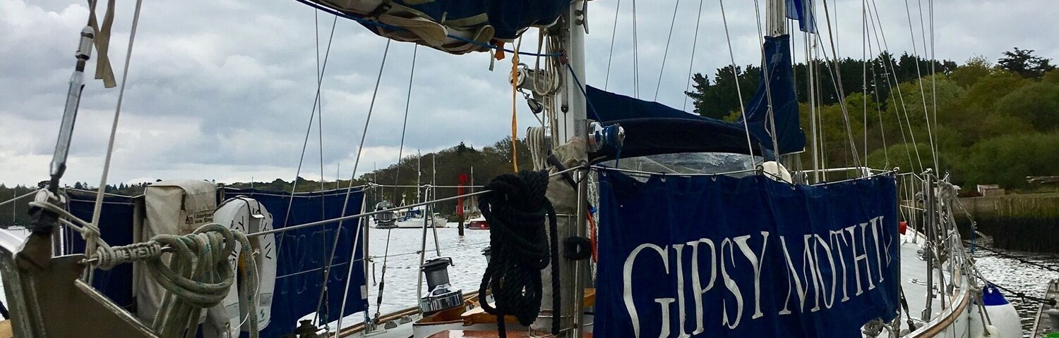 A sailboat docked at a marina with a blue tarp labeled "GIPSY MOTHER" and a cloudy sky in the background.