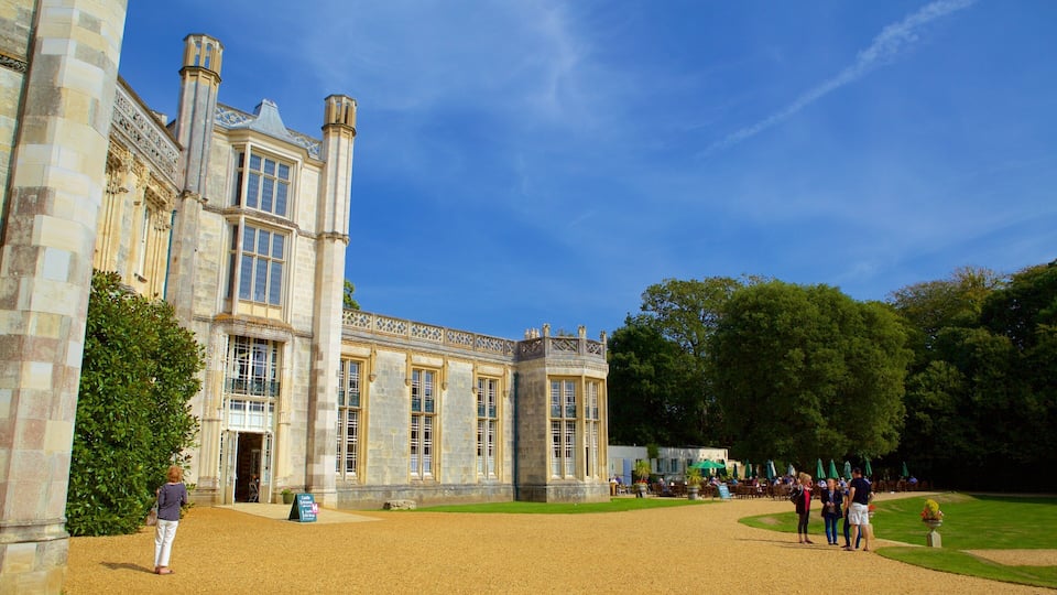 A historic building with large windows and stone columns, surrounded by a gravel courtyard and lush greenery.