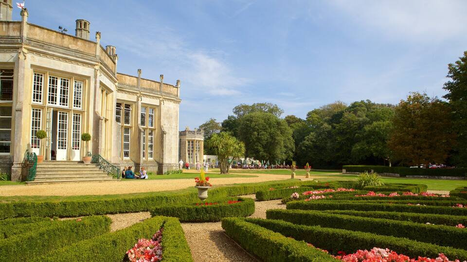 A historic building with large windows and a formal garden with neatly trimmed hedges and flower beds.