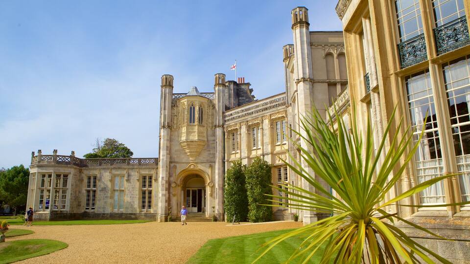 A historic building with a large entrance, a flag, and a well-maintained garden.