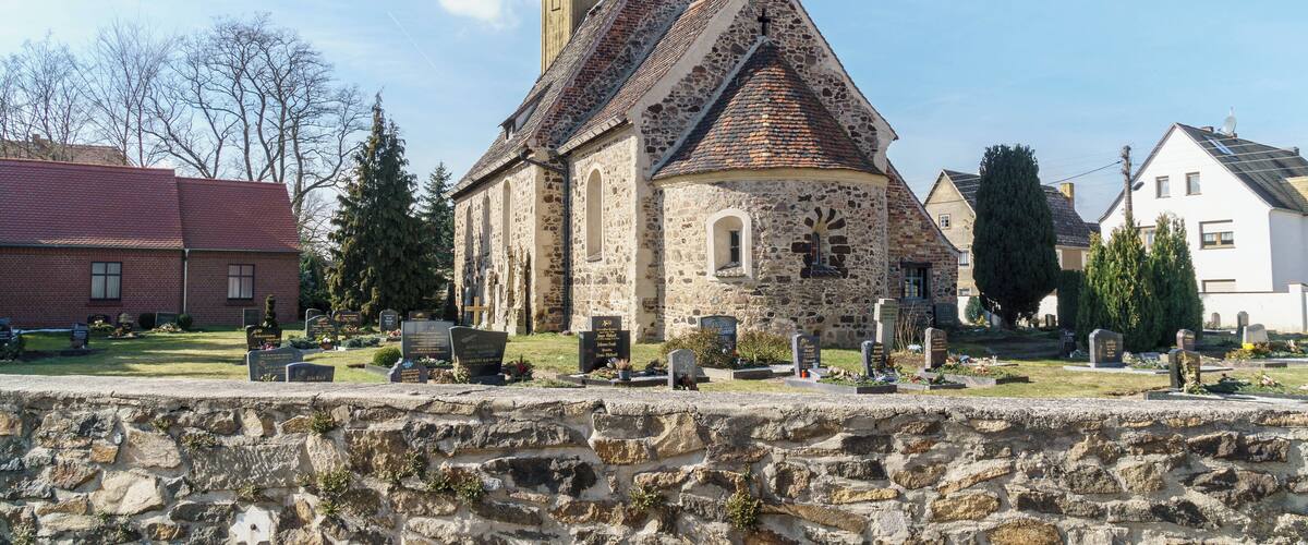 Una iglesia con una torre del reloj y un cementerio en la parte delantera.