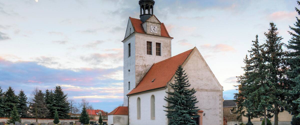 A church with a tall steeple and a clock tower, surrounded by gravestones and trees.