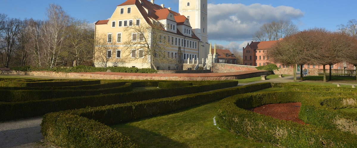 A historic building with a tower, surrounded by manicured gardens and trees.