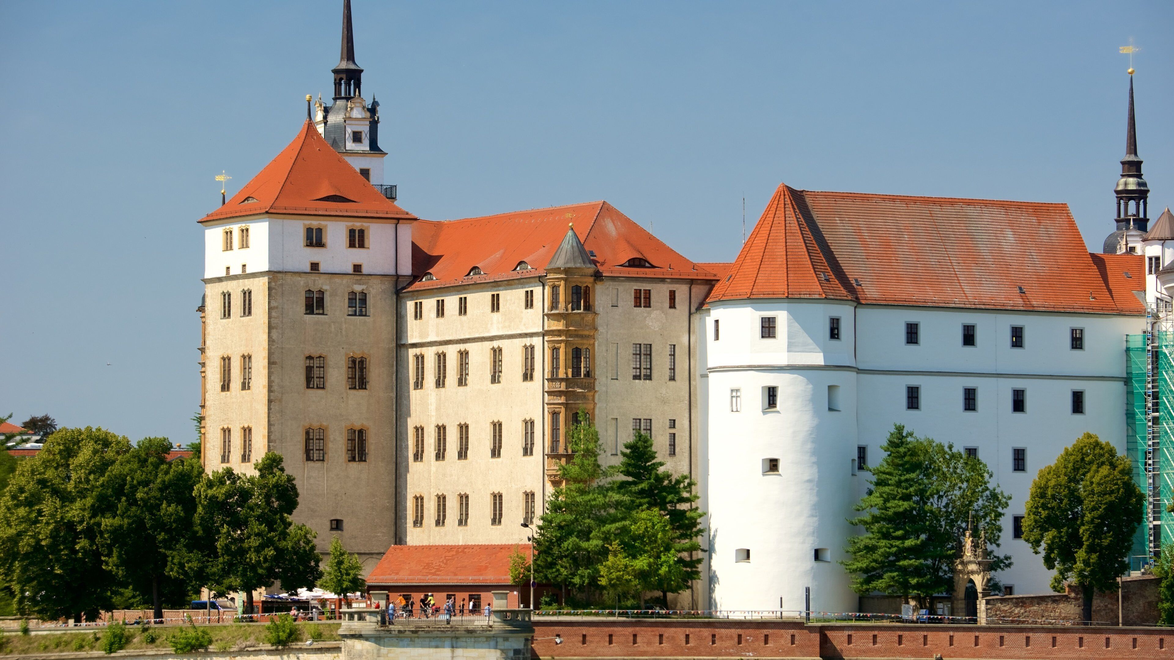 A historic building with a red-tiled roof, a tower with a spire, and a white building with a corner turret.