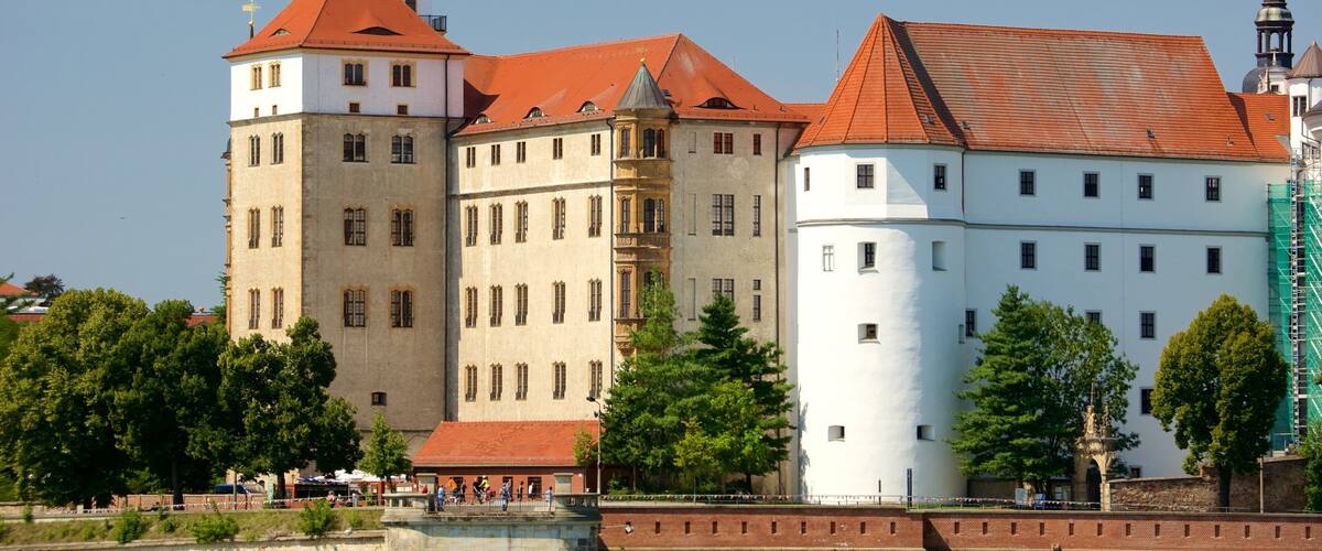 A historic building with a red-tiled roof, a tower with a spire, and a white building with a corner turret.