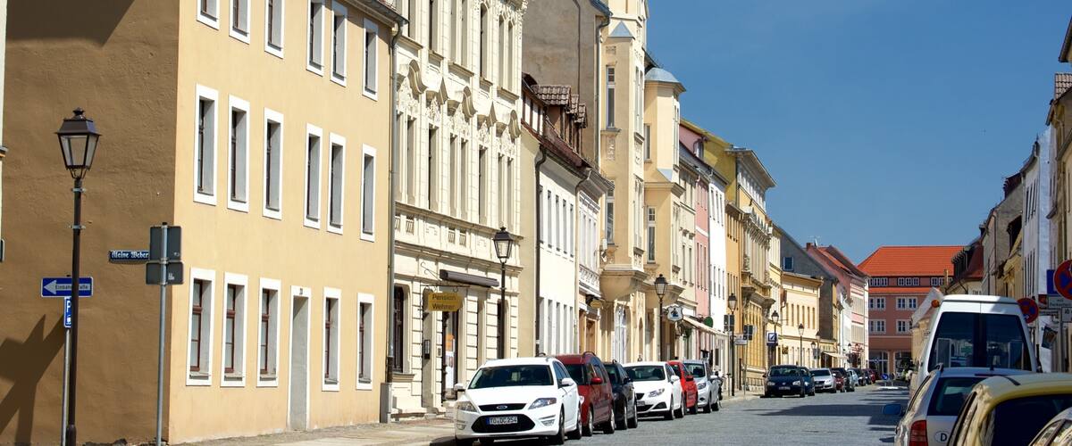 A street lined with historic buildings, parked cars, and street lamps.