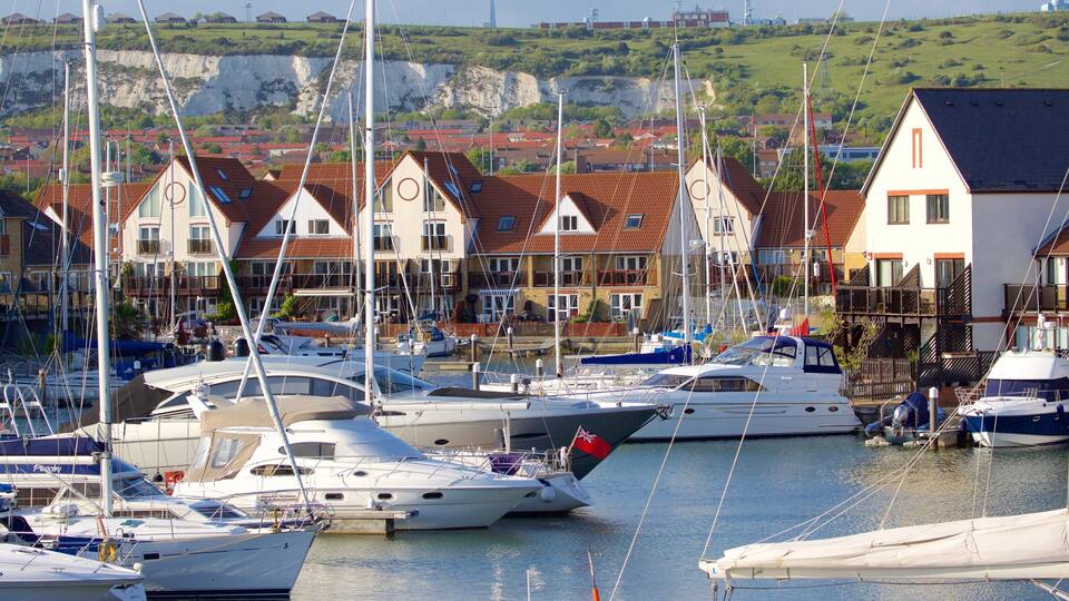 Ein Yachthafen mit mehreren angossenen Yachten, umgeben von Häusern mit roten Ziegeldächern und einer Klippe im Hintergrund.