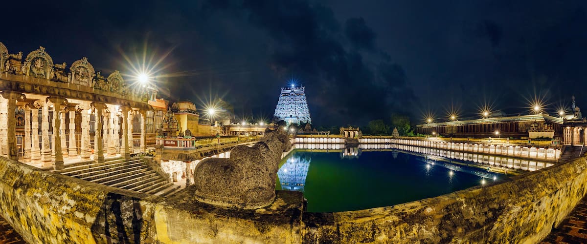 A night view of a historic site with illuminated structures, a large central building, and a reflective water body.