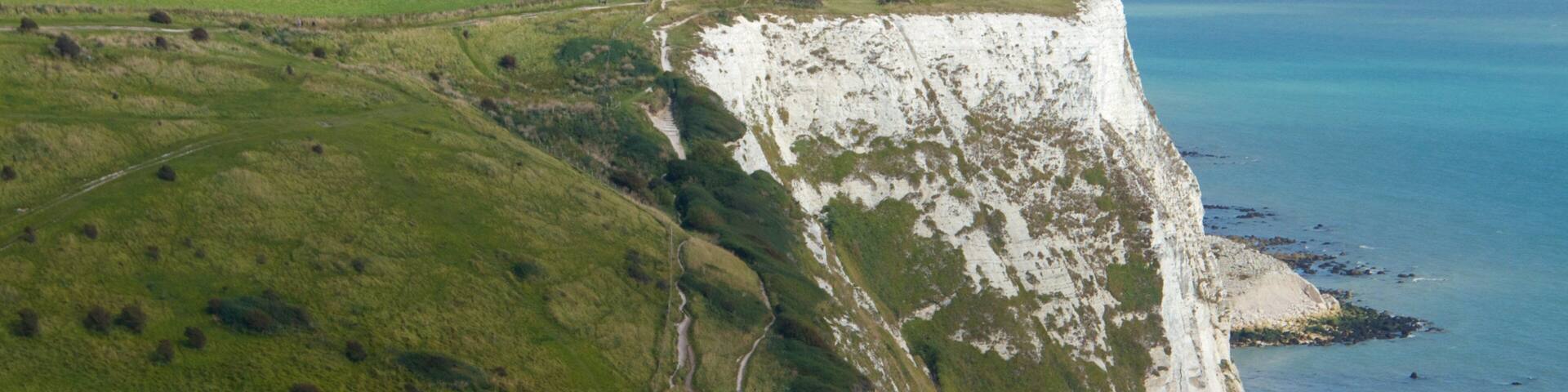 A coastal cliff with white chalk formations and green fields.