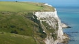 A coastal cliff with white chalk formations and green fields.