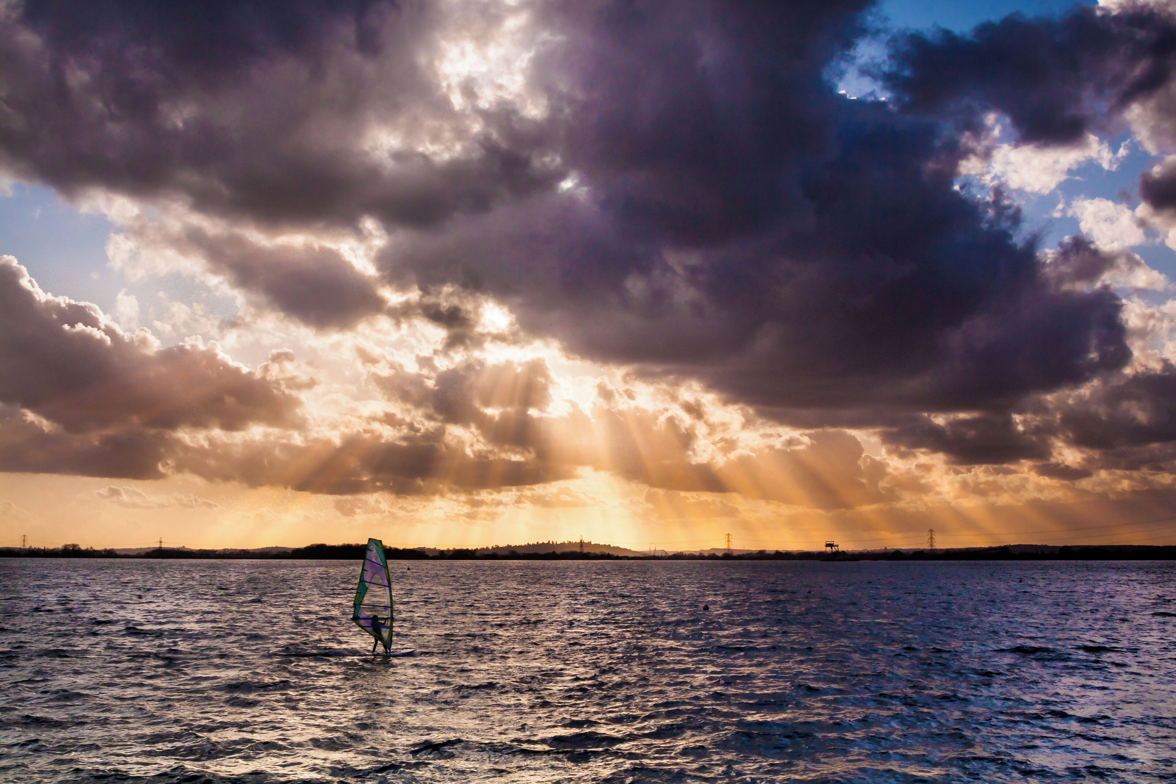 A person windsurfing on a body of water with a dramatic sky.