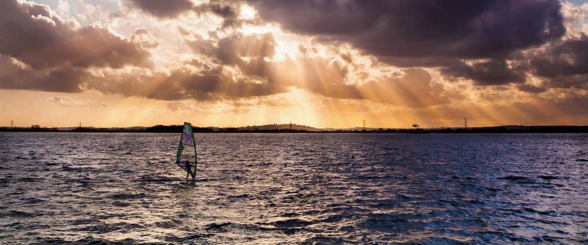 A person windsurfing on a body of water with a dramatic sky.