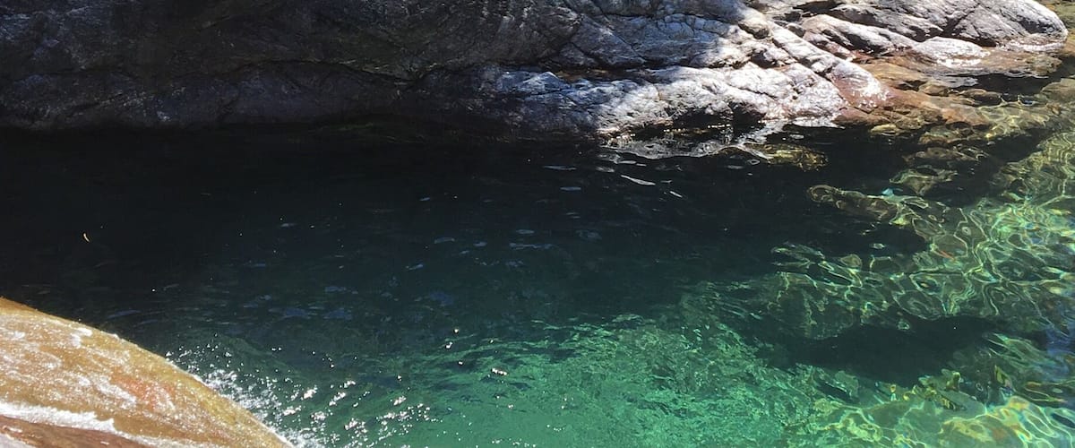 A rocky stream with clear water, surrounded by large boulders and sparse vegetation.