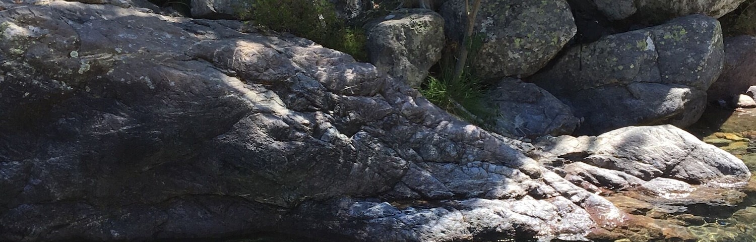 A rocky stream with clear water, surrounded by large boulders and sparse vegetation.