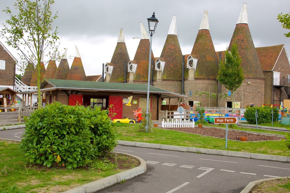 A village with conical-roofed buildings, a red-roofed shop, and a sign pointing to 'Hop Farm'.